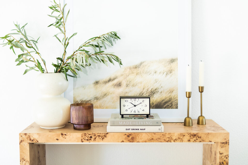Light wood console table from Target with decorative brass candles, plants, clock, coffee table books, and picture frame by Natalie Barnas Interiors based in San Marcos, California.